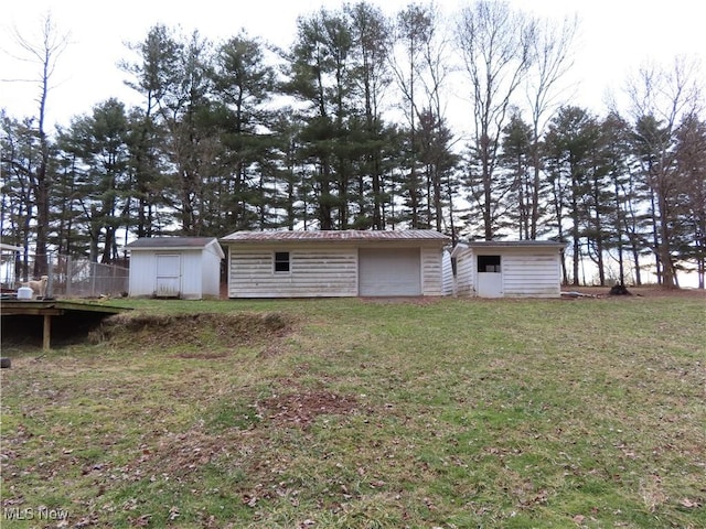 back of house featuring a storage unit, metal roof, a lawn, and an outbuilding