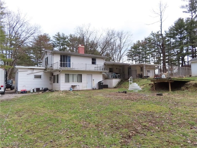 back of property with a balcony, a yard, and a chimney