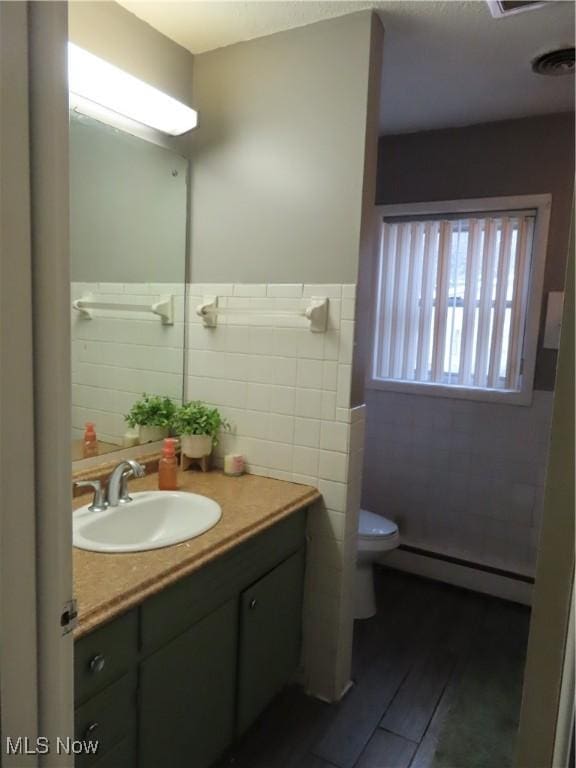 bathroom with wainscoting, toilet, vanity, a baseboard heating unit, and tile walls