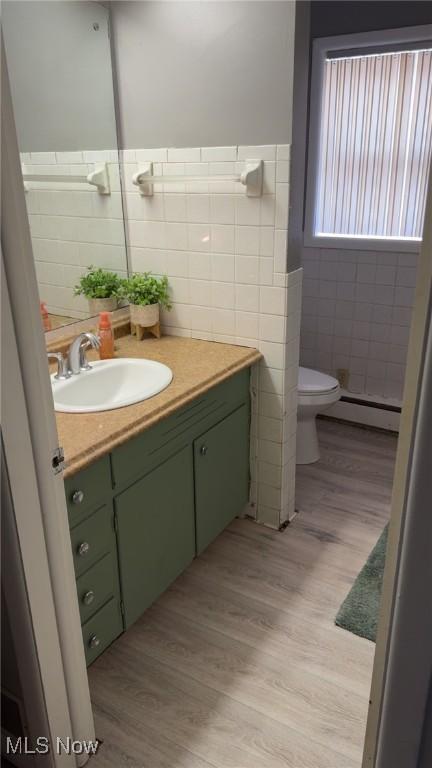 bathroom featuring a baseboard heating unit, toilet, vanity, wood finished floors, and tile walls