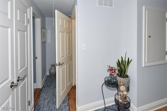 hall with visible vents, baseboards, and wood finished floors