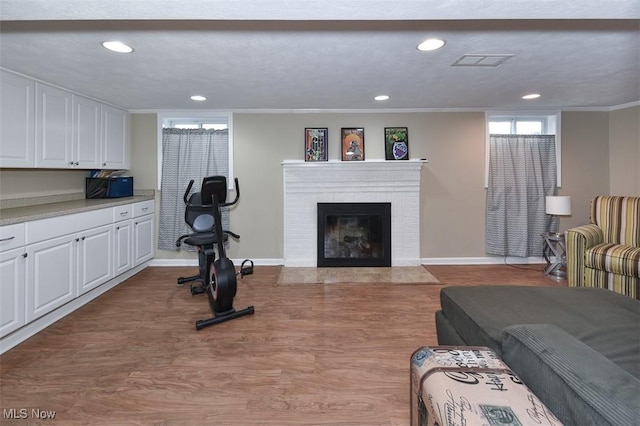 living area with visible vents, ornamental molding, wood finished floors, a brick fireplace, and recessed lighting