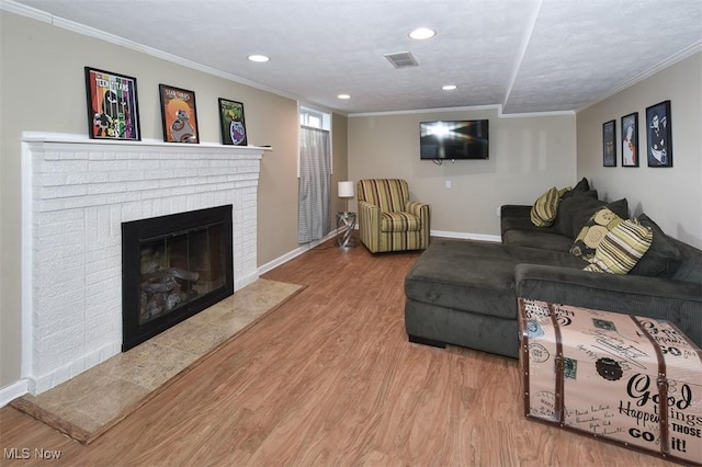 living area with a brick fireplace, visible vents, wood finished floors, and ornamental molding