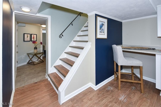 interior space with a textured ceiling, wood finished floors, baseboards, built in study area, and crown molding