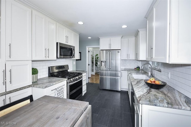 kitchen with light stone counters, appliances with stainless steel finishes, white cabinets, and a sink