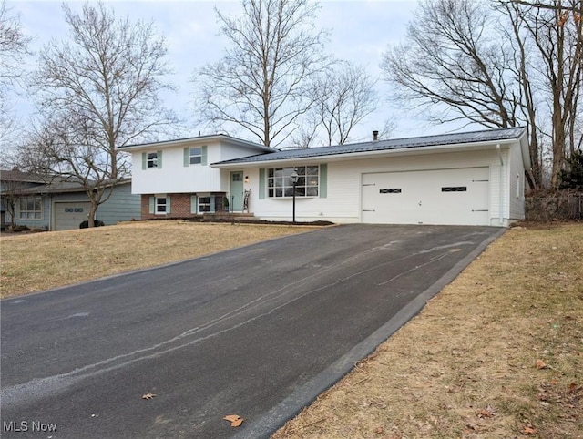 tri-level home with metal roof, aphalt driveway, an attached garage, a front lawn, and brick siding