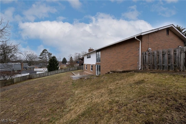 view of side of property with a yard, brick siding, a chimney, and a fenced backyard