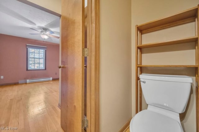 bathroom with ceiling fan, toilet, a baseboard heating unit, wood finished floors, and baseboards