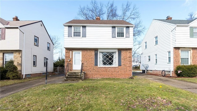 colonial-style house featuring a front yard, a chimney, aphalt driveway, and brick siding