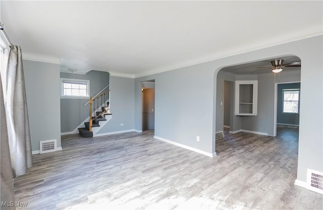 spare room with arched walkways, wood finished floors, visible vents, stairway, and a wealth of natural light