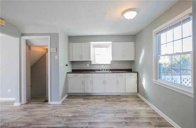 kitchen with dark countertops, white cabinets, light wood-style flooring, and baseboards