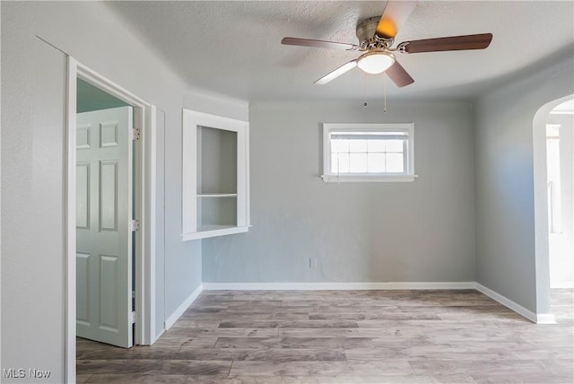 spare room with arched walkways, a textured ceiling, wood finished floors, and baseboards