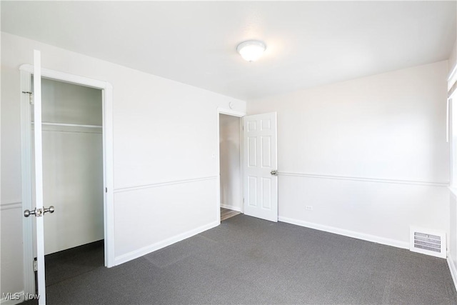 unfurnished bedroom with a closet, visible vents, dark carpet, and baseboards