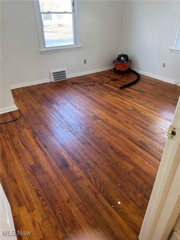 empty room featuring baseboards, visible vents, and hardwood / wood-style floors