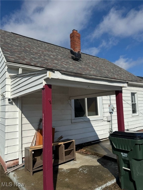 back of property with a patio area, roof with shingles, and a chimney