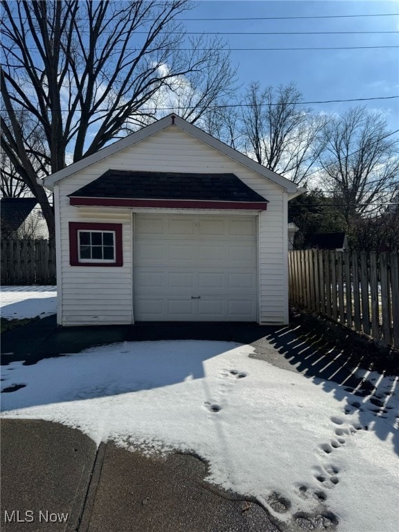 snow covered garage with a garage, fence, and driveway