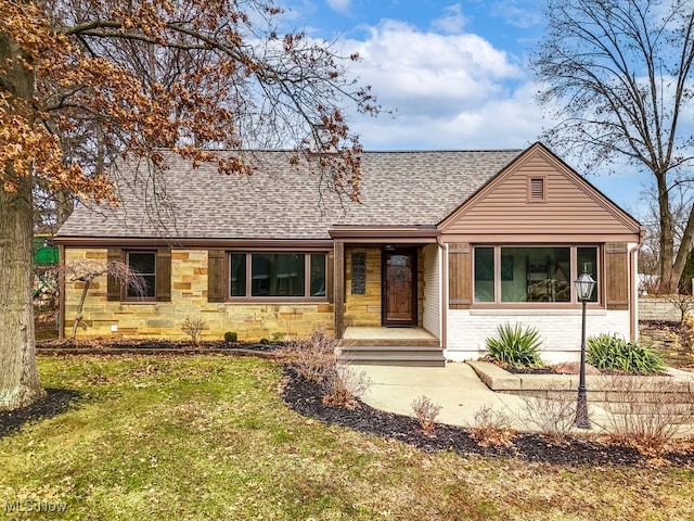 single story home with stone siding, a shingled roof, and a front lawn