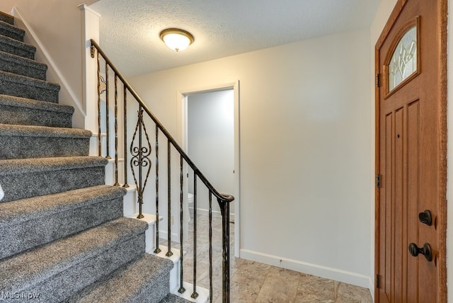 foyer entrance featuring stairway, a textured ceiling, and baseboards