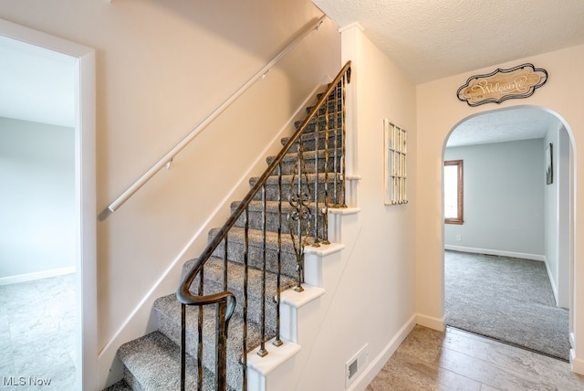 staircase featuring arched walkways, visible vents, a textured ceiling, and baseboards