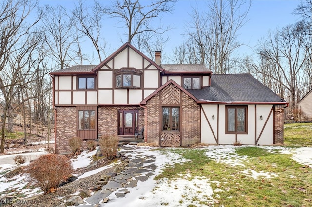 tudor home featuring brick siding, roof with shingles, a chimney, and stucco siding