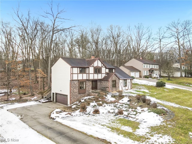 tudor house featuring a garage, driveway, a chimney, and brick siding