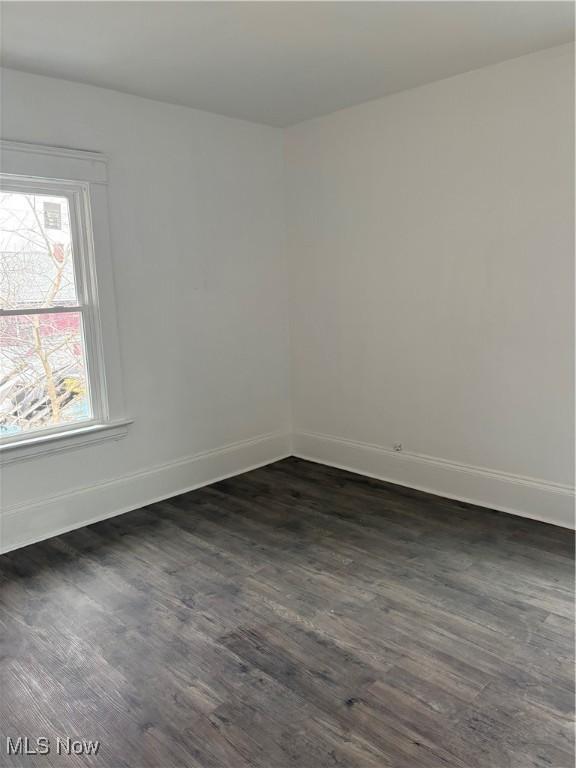 unfurnished room with baseboards and dark wood-type flooring