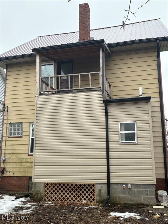 view of side of property with a chimney, metal roof, and a balcony