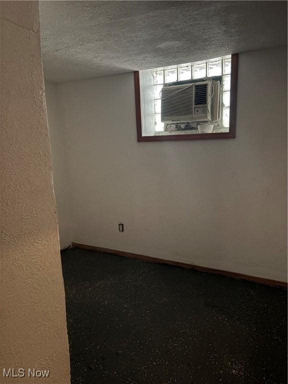 empty room featuring a textured ceiling, cooling unit, and baseboards