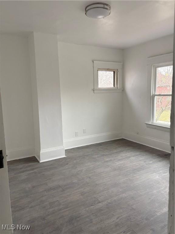 spare room with baseboards and dark wood-style flooring