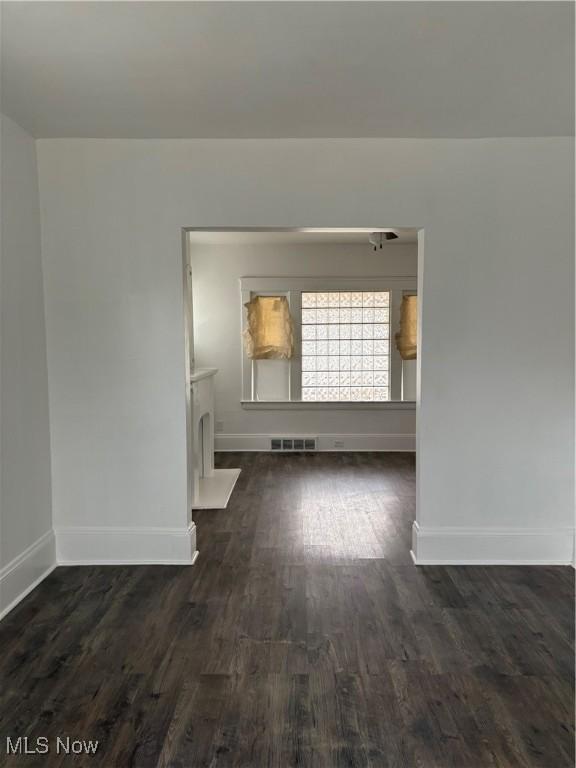 empty room with dark wood finished floors, visible vents, and baseboards