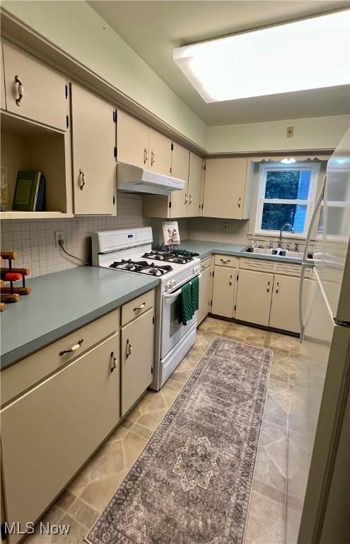 kitchen featuring under cabinet range hood, tasteful backsplash, white appliances, and a sink