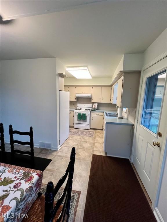 kitchen featuring white appliances, a sink, visible vents, and under cabinet range hood