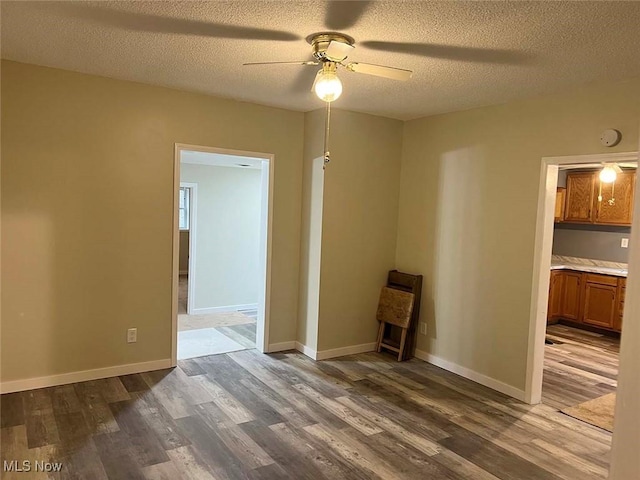 empty room featuring a textured ceiling, dark wood finished floors, a ceiling fan, and baseboards