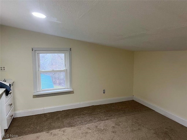 unfurnished room featuring a textured ceiling, vaulted ceiling, carpet, and baseboards