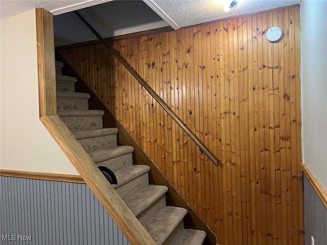 stairs with wooden walls, a textured ceiling, and wainscoting