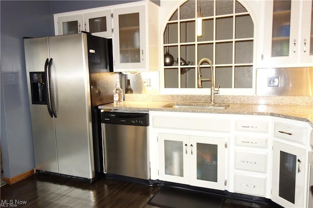 kitchen featuring light stone counters, dark wood-type flooring, stainless steel appliances, white cabinetry, and a sink