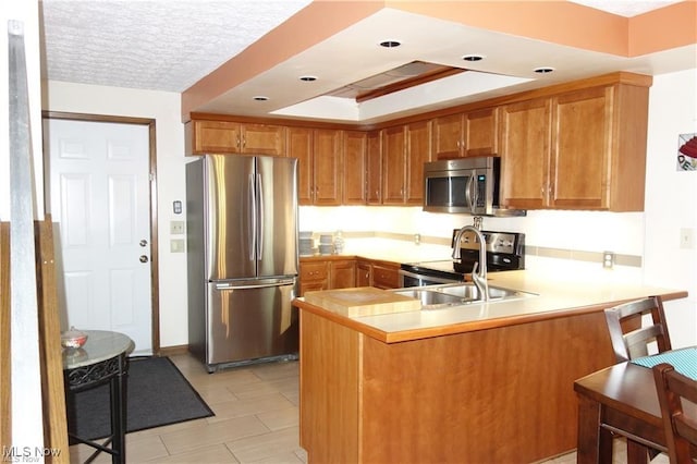 kitchen with brown cabinetry, appliances with stainless steel finishes, a peninsula, light countertops, and a textured ceiling