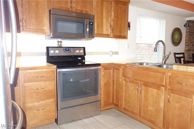 kitchen featuring appliances with stainless steel finishes, brown cabinets, light countertops, and a sink