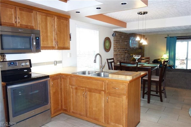 kitchen with appliances with stainless steel finishes, brown cabinets, open floor plan, a peninsula, and a sink