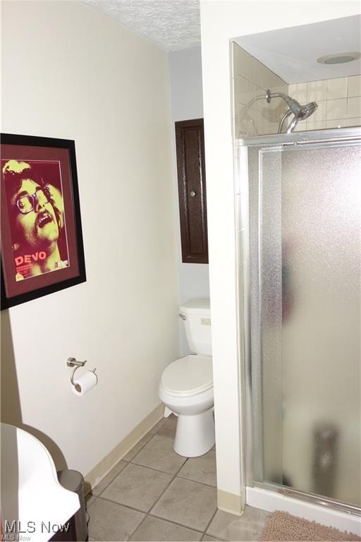 bathroom with toilet, a shower stall, a textured ceiling, and tile patterned floors