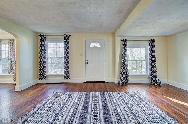 entryway with a wealth of natural light, arched walkways, and wood finished floors