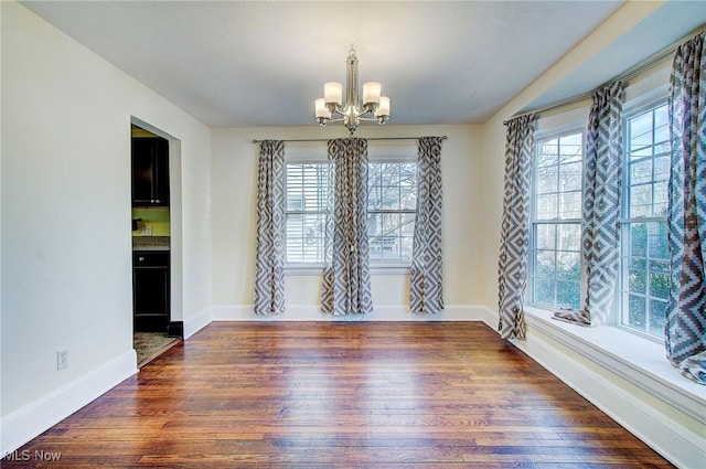 unfurnished room with an inviting chandelier, plenty of natural light, and wood finished floors