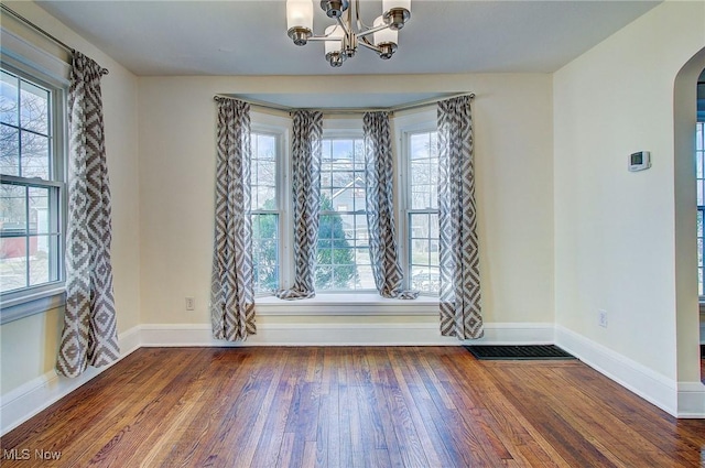 unfurnished dining area featuring arched walkways, wood-type flooring, a wealth of natural light, and baseboards