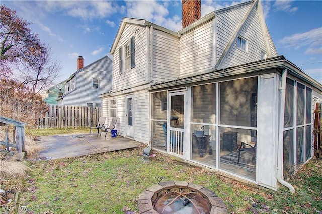 rear view of property with a patio, a fire pit, fence, a sunroom, and a chimney