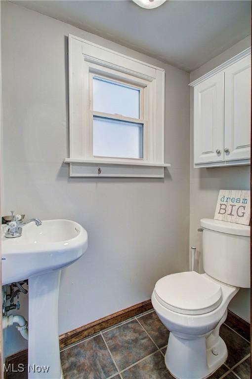 half bath featuring toilet, baseboards, and a sink