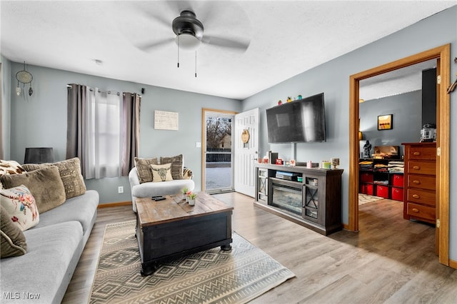 living area featuring baseboards, ceiling fan, wood finished floors, a textured ceiling, and a fireplace