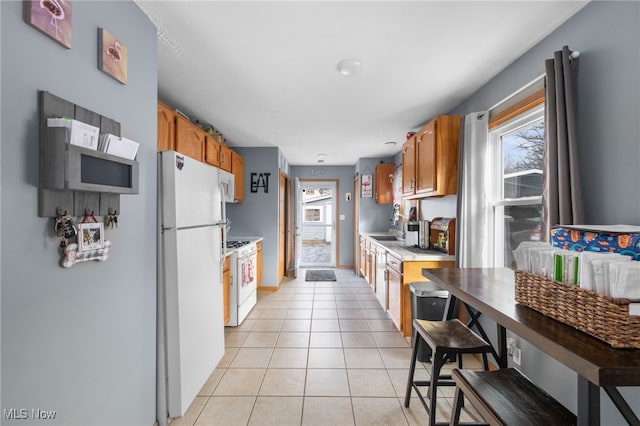 kitchen with light countertops, white appliances, brown cabinetry, and light tile patterned flooring