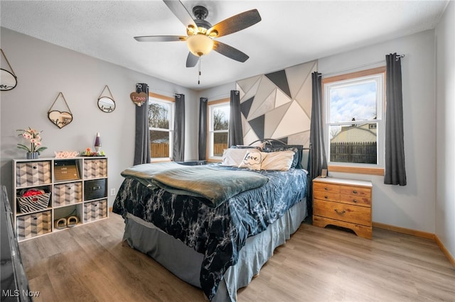 bedroom with light wood-style floors, a textured ceiling, baseboards, and a ceiling fan