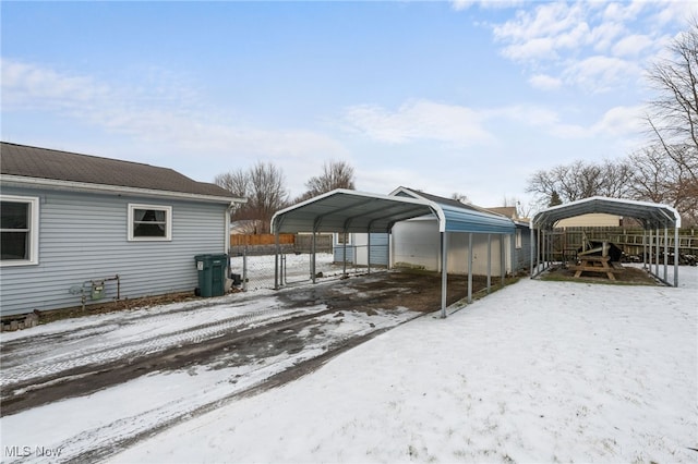 snow covered property with a detached carport, a gate, and fence