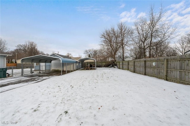 snowy yard with a carport and fence